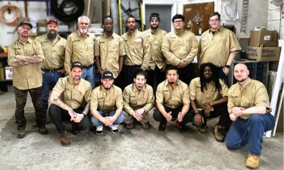 Group of workers in tan uniforms posing in a warehouse, some standing and some kneeling.