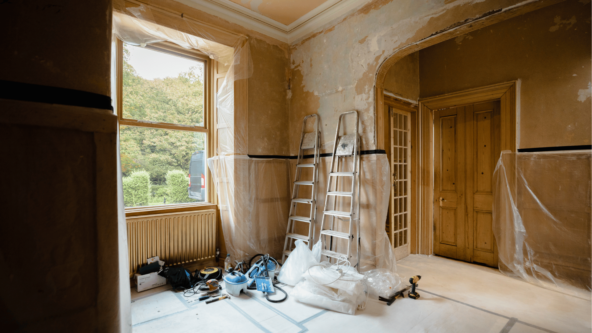 An empty room with a ladder and tools on the floor.