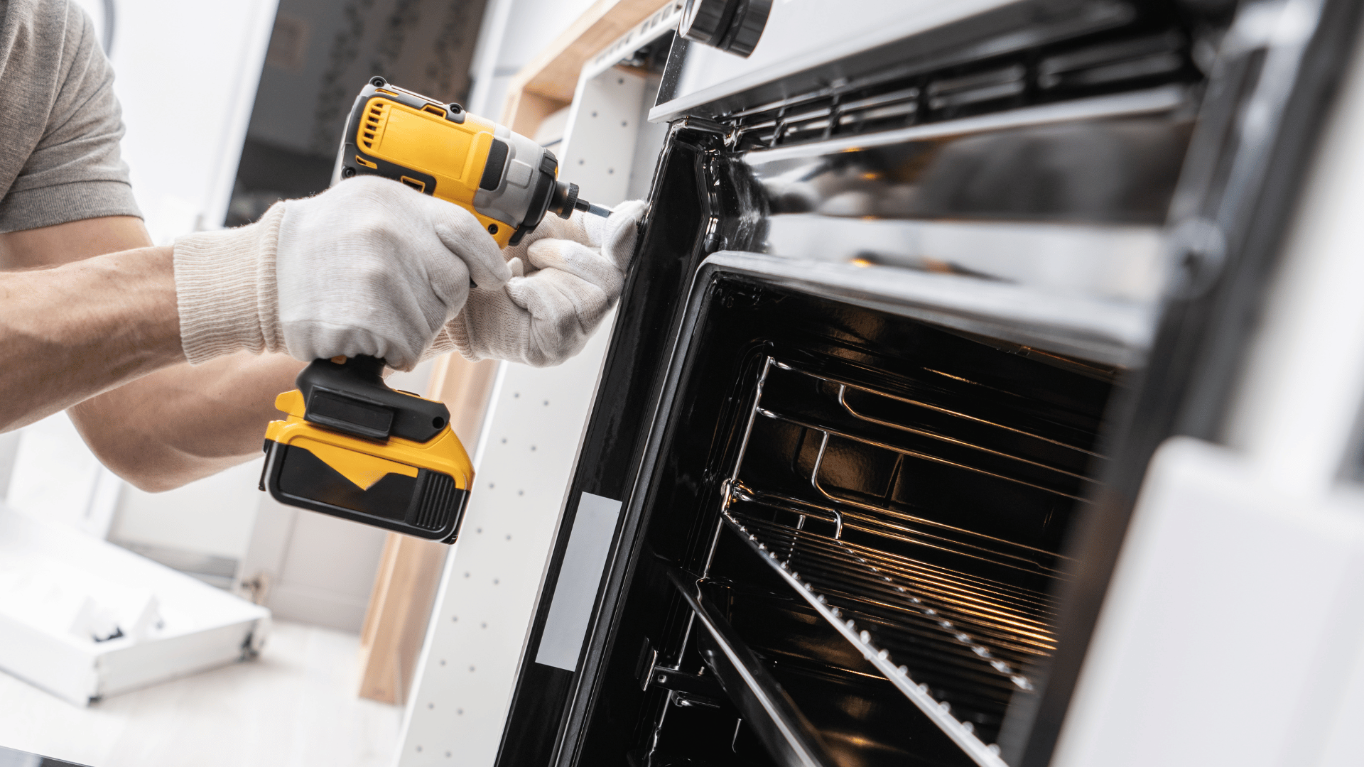 A man is fixing an oven with a drill.