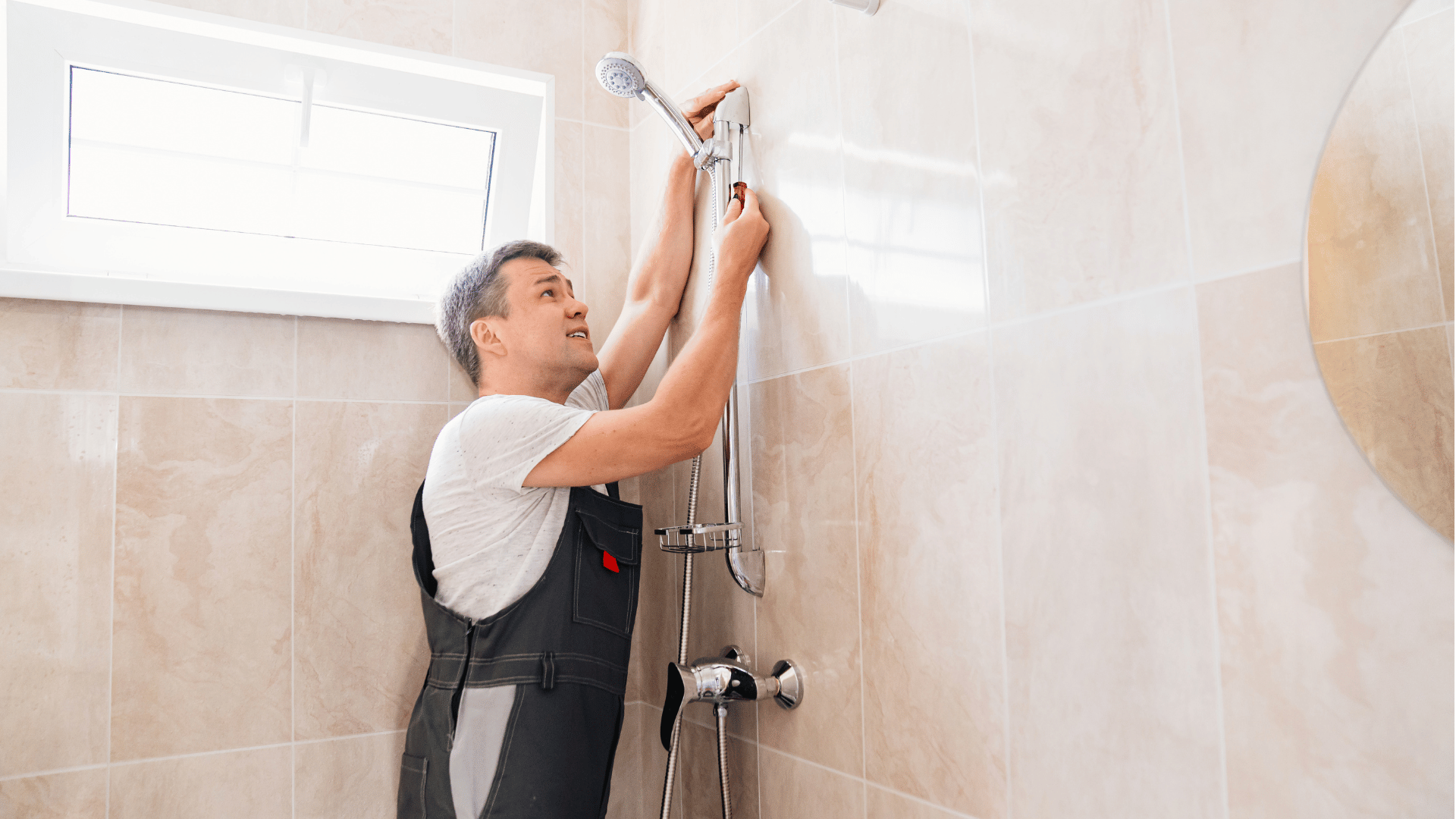 A man is installing a shower head in a bathroom.