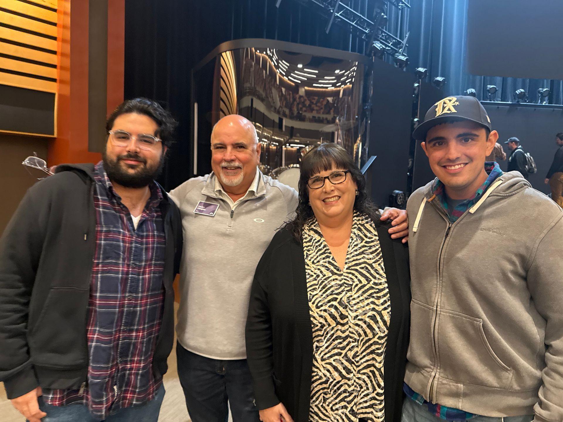 Four smiling people stand side-by-side in a studio or stage setting, posing for a group photo.