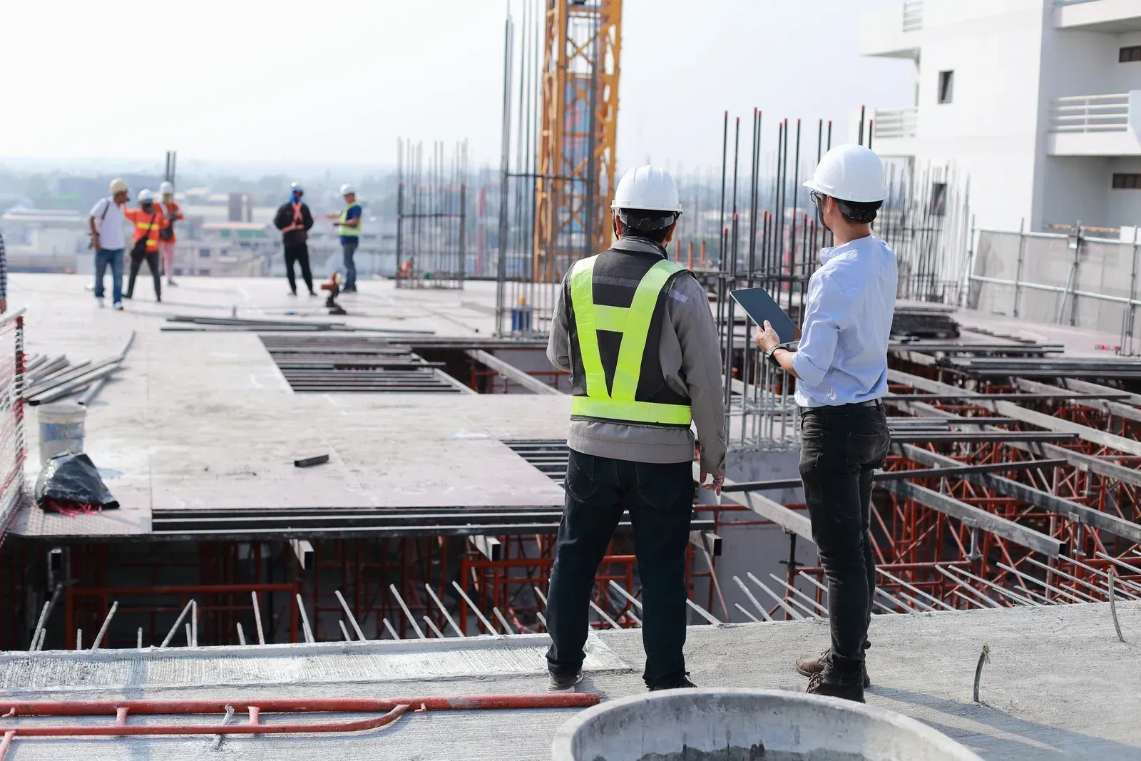 Two construction workers are standing on top of a building under construction.