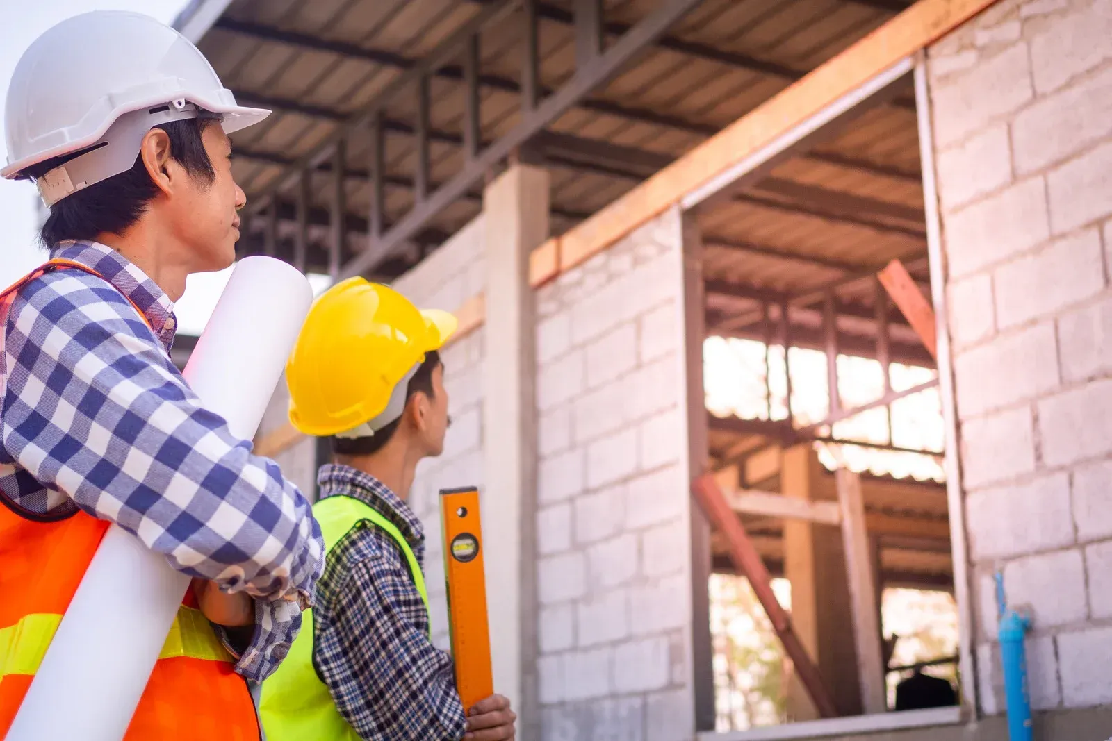 Two construction workers are standing in front of a building under construction.