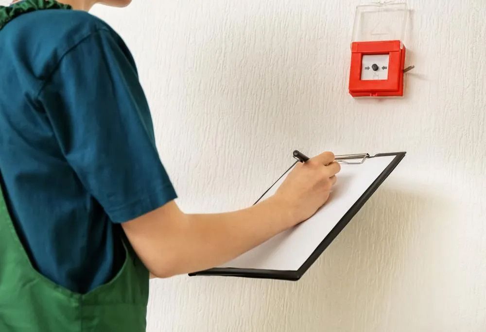 Person in Green Overalls Inspecting a Fire Alarm — FNQ Smoke Alarms & Maintenance in Goldsborough, QLD
