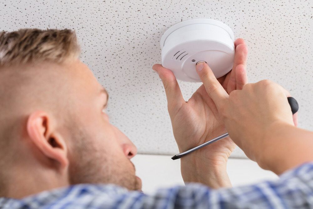 Man Using a Screwdriver to Install a White Smoke Detector — FNQ Smoke Alarms & Maintenance in Goldsborough, QLD