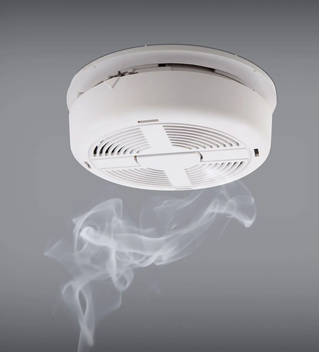 White Smoke Detector on a Gray Ceiling, Emitting Smoke — FNQ Smoke Alarms & Maintenance in Port Douglas, QLD