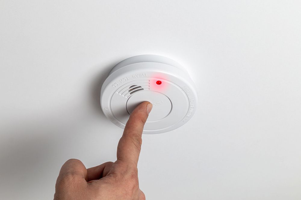 A Person's Finger Pressing a Test Button on a White Smoke Detector — FNQ Smoke Alarms & Maintenance in Yungaburra, QLD