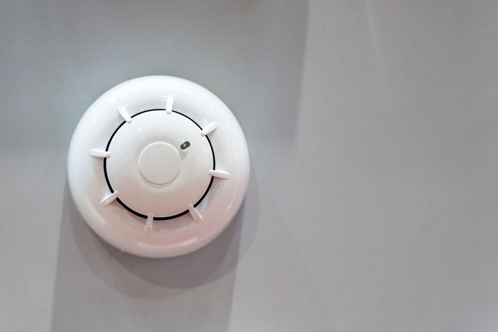 White Smoke Detector Mounted on a Gray Wall — FNQ Smoke Alarms & Maintenance in Goldsborough, QLD