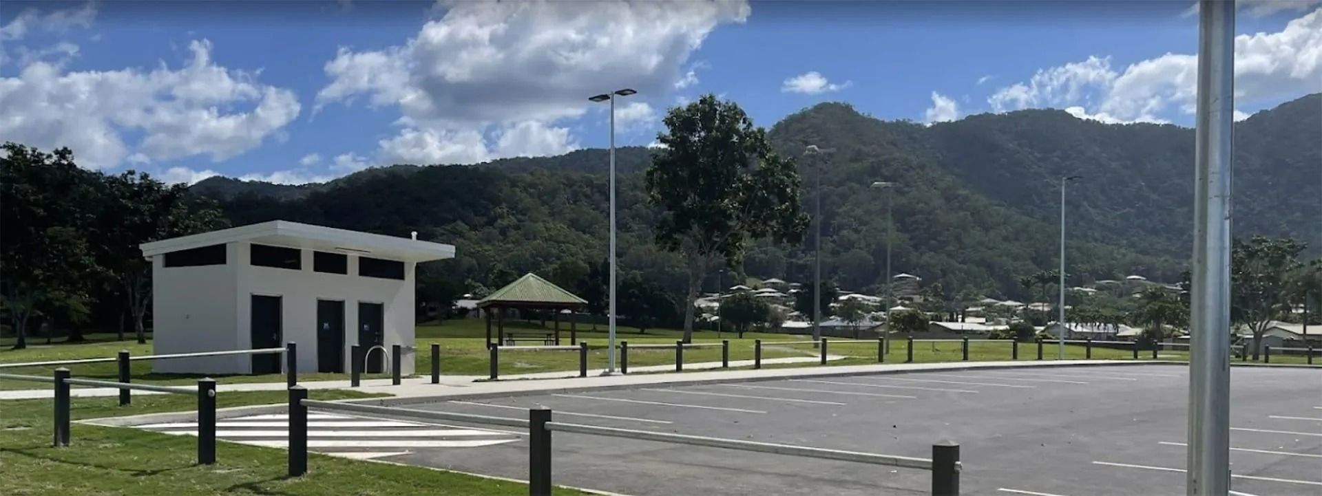 A white restroom building and parking lot in front of mountains — FNQ Smoke Alarms & Maintenance in Mount Sheridan, QLD
