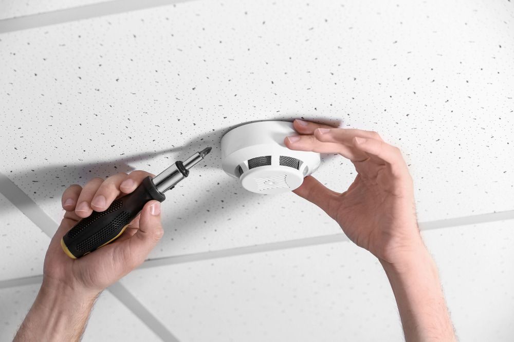 Person Installing a White Smoke Detector — FNQ Smoke Alarms & Maintenance in Cairns, QLD