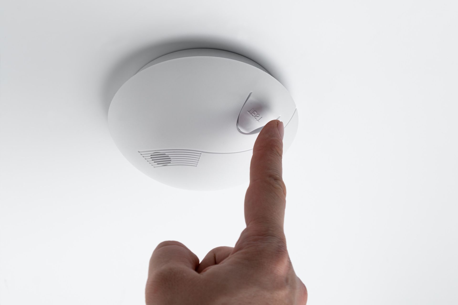 Hand Pressing a Button on a White Ceiling-mounted Smoke Detector — FNQ Smoke Alarms & Maintenance in Mareeba, QLD