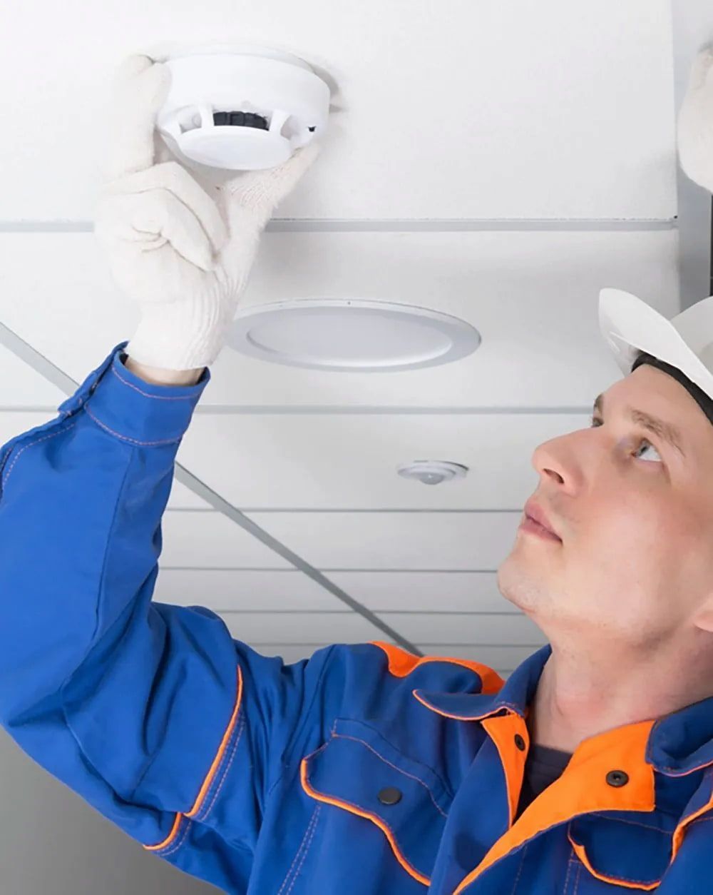 Man in Blue Jumpsuit Installing a Smoke Detector on a White Ceiling — FNQ Smoke Alarms & Maintenance in Innisfail, QLD