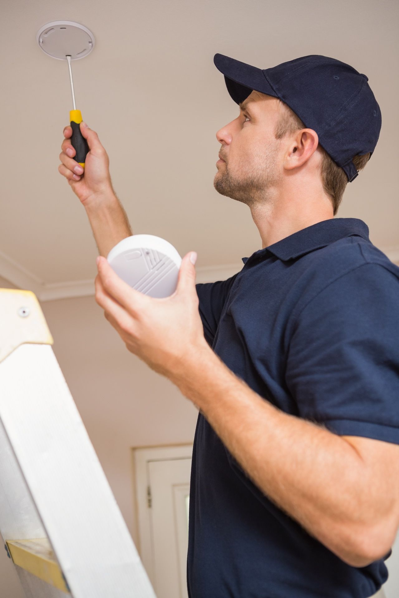 Hands Installing a Smoke Detector on a White Ceiling — FNQ Smoke Alarms & Maintenance in Goldsborough, QLD
