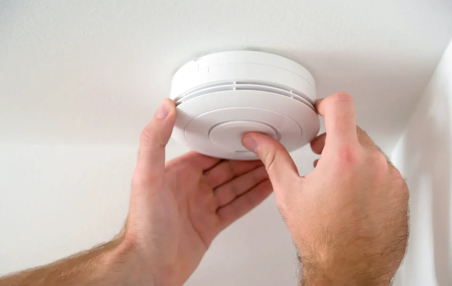 Hand Pressing Test Button on a White Smoke Detector — FNQ Smoke Alarms & Maintenance in Goldsborough, QLD