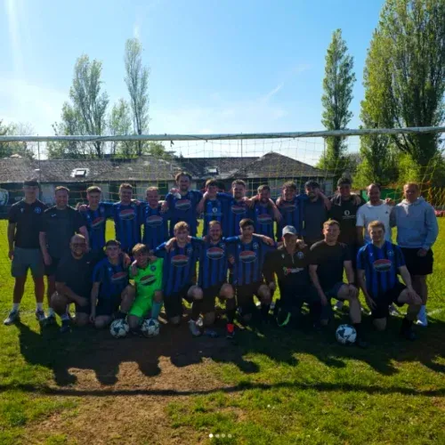 Soccer team posing for a group photo on a sunny field, wearing blue and black uniforms.