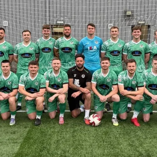 Football team in green kits posing together on an indoor pitch with a football.
