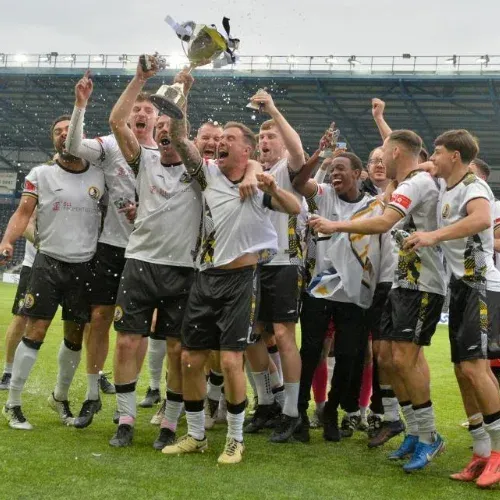 Football team celebrating on the pitch as a player lifts a trophy above his head.