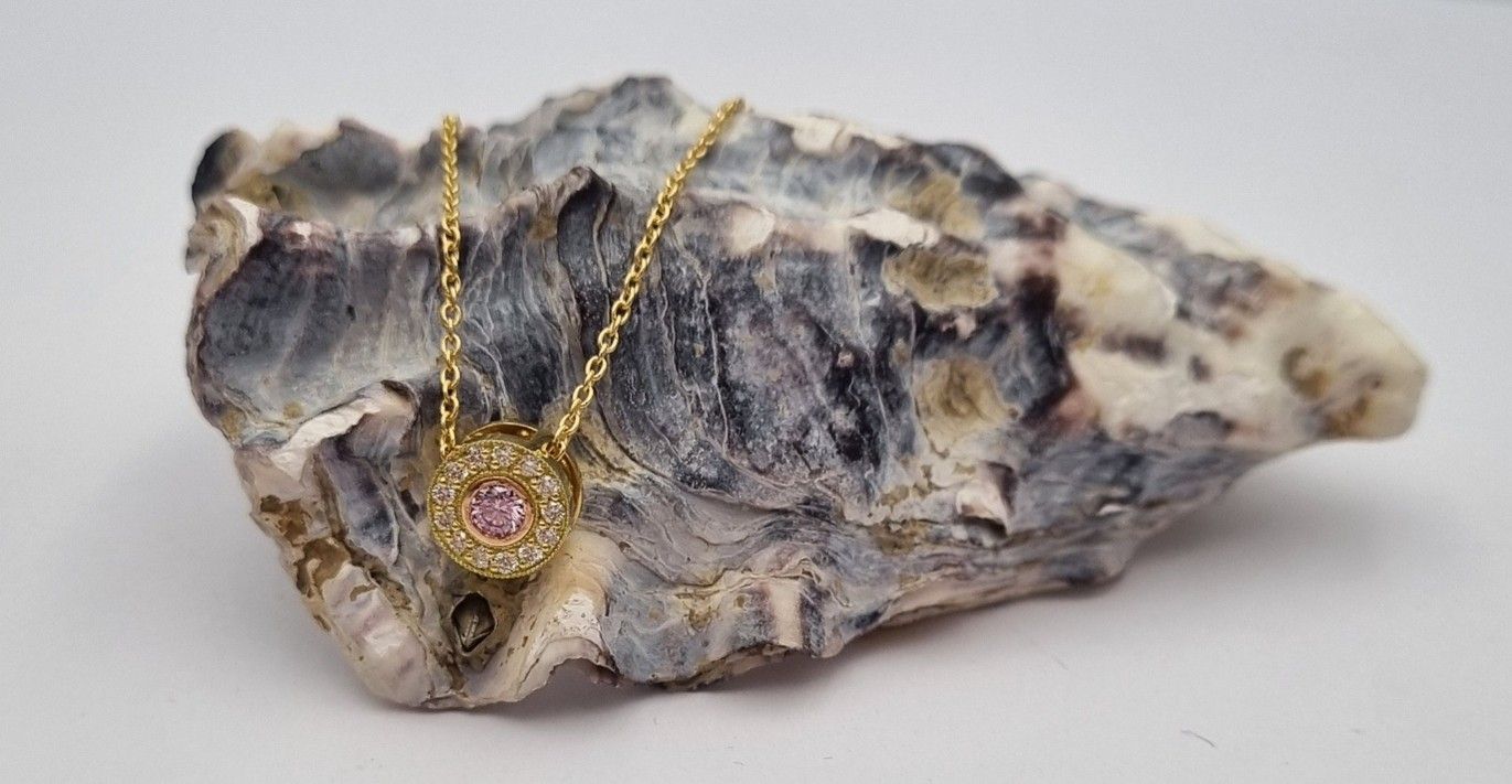 Gold necklace with pink gem on oyster shell.