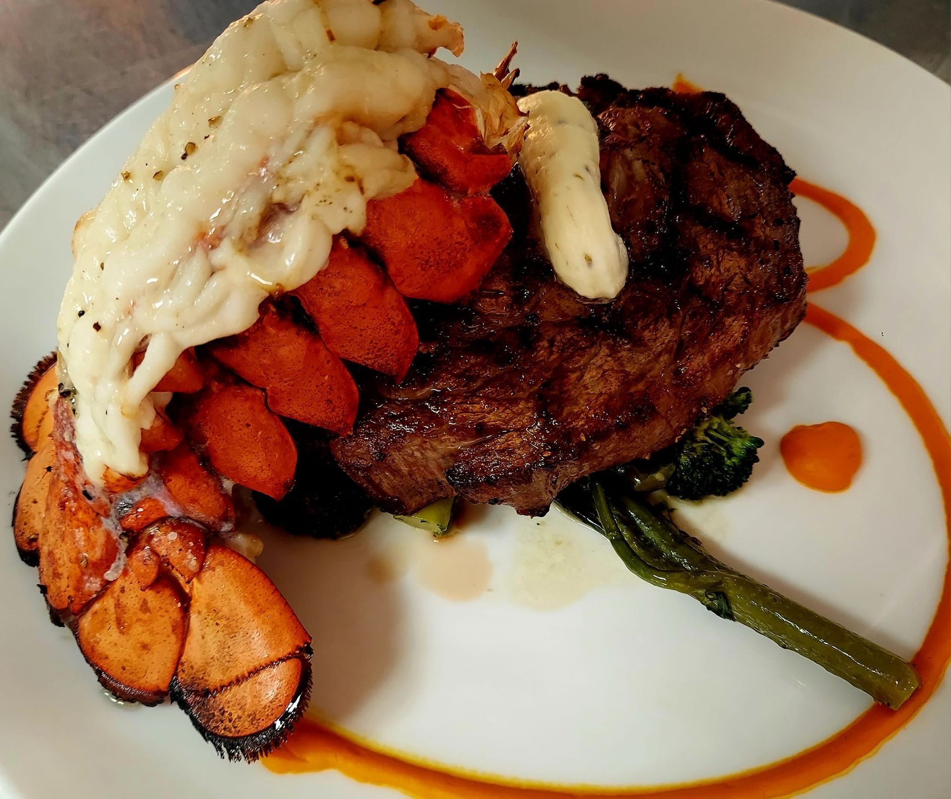 A surf and turf plate featuring a grilled steak topped with compound butter next to a lobster tail and broccolini.