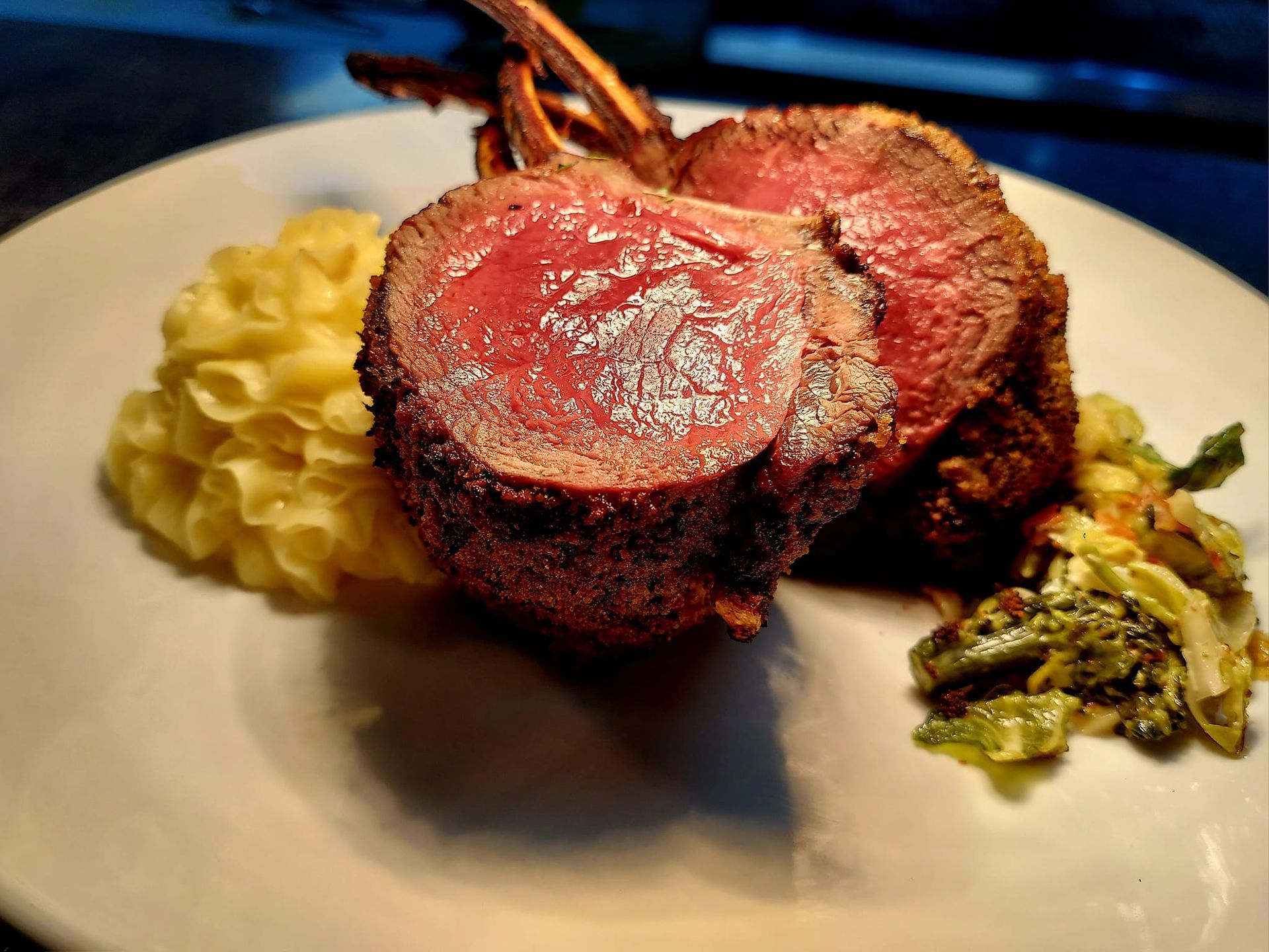 A rack of medium-rare lamb chops served with a side of creamy mashed potatoes and sautéed green vegetables on a plate.