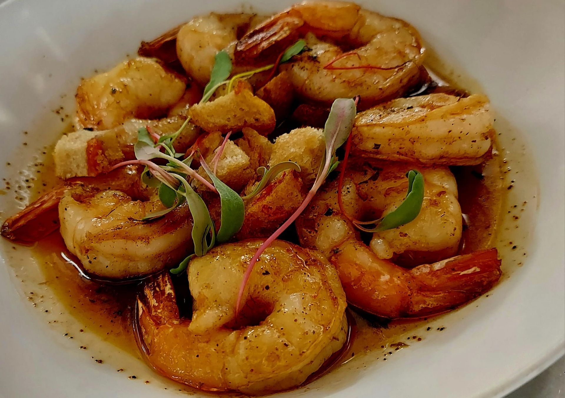 A white bowl containing sautéed shrimp in a seasoned butter sauce, garnished with fresh microgreens.