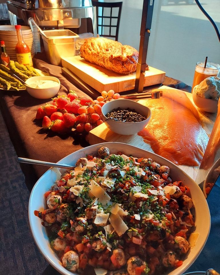 A buffet table featuring a large bowl of salad with mozzarella pearls, smoked salmon, strawberries, and rustic bread.