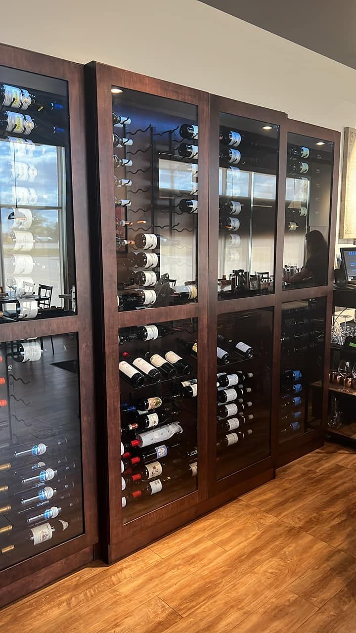 A wall of dark wood wine cabinets with glass doors, filled with rows of wine bottles against a plain wall on a wood floor.