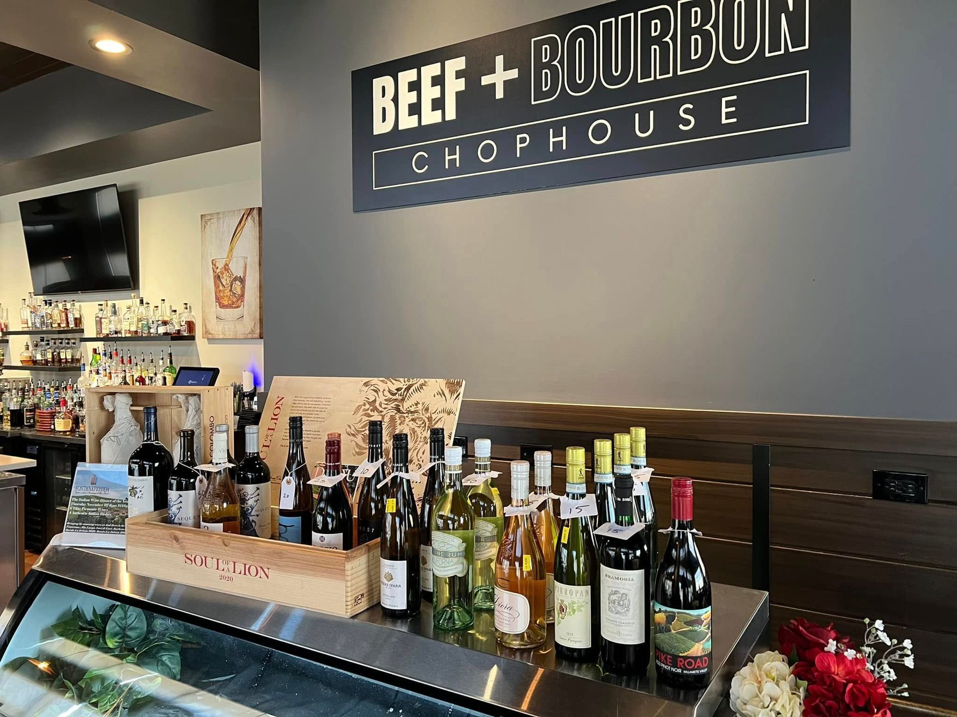 A Beef + Bourbon Chophouse restaurant interior with a display of various wine bottles on a counter in front of a sign.
