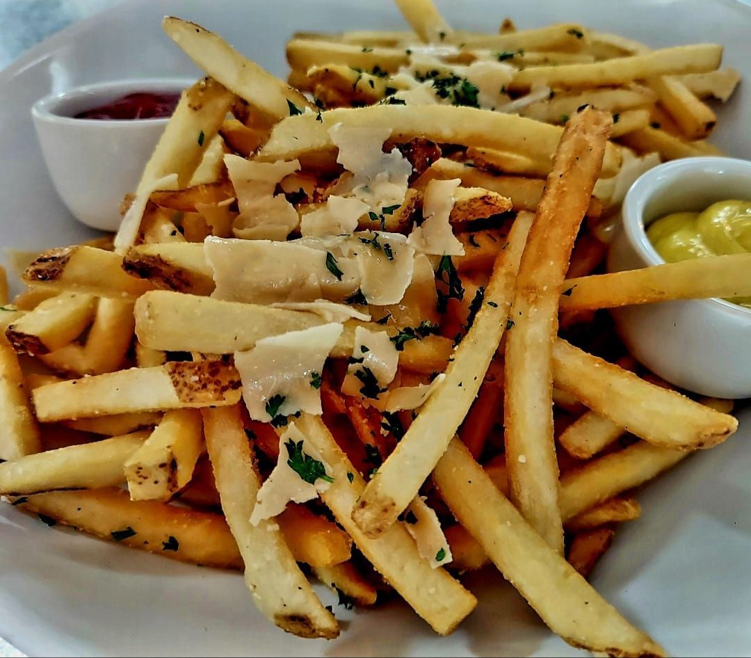 A plate of thin, golden fries topped with shaved Parmesan cheese and herbs, served with small cups of red and yellow sauce.