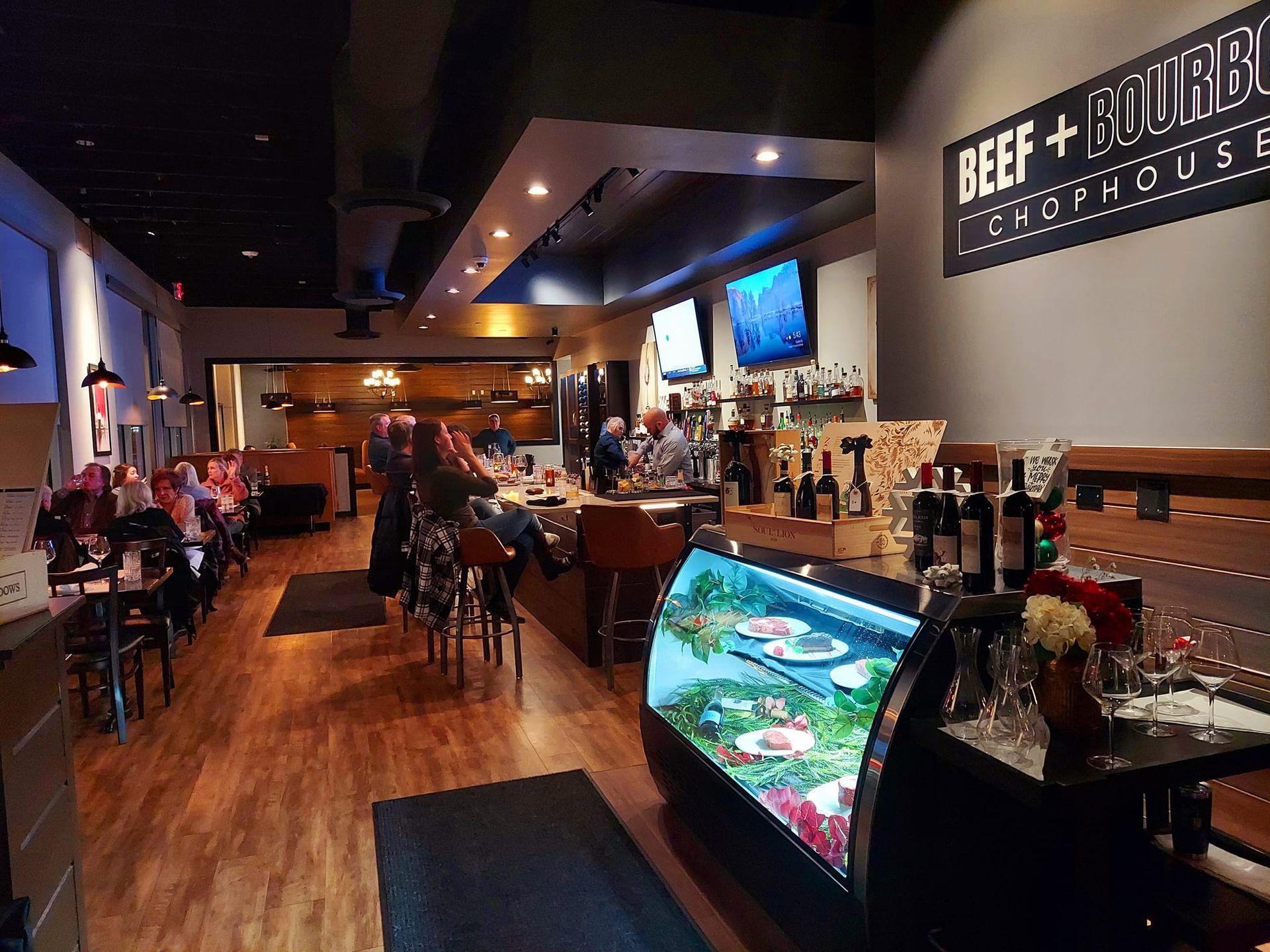 A view of a modern restaurant interior featuring a bar with stools, a refrigerated food display, and ambient lighting.