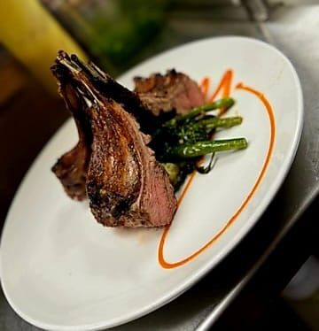 Two seared lamb chops served with green vegetables and a decorative swirl of orange sauce on a white plate.