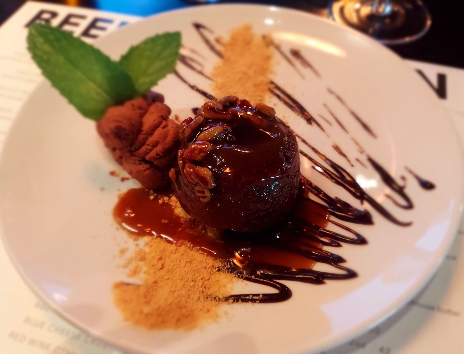 A chocolate lava cake topped with pecans, served with caramel sauce, a chocolate truffle, mint, and cookie crumbs.
