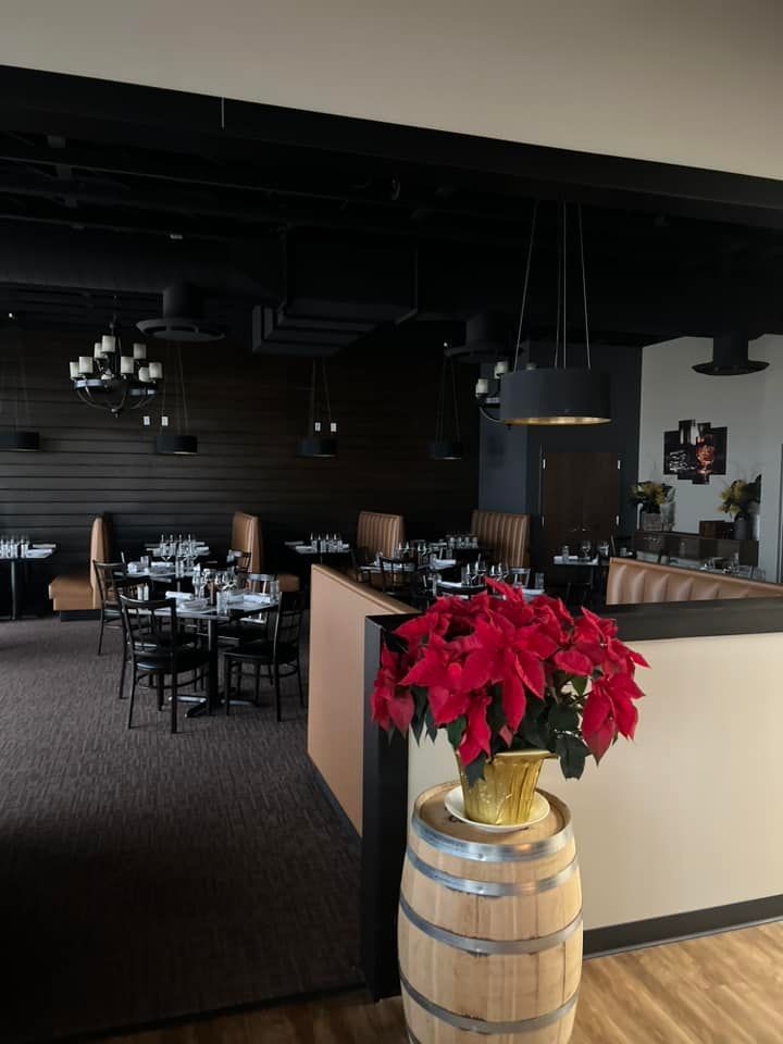 A poinsettia plant sits on a wooden barrel in the foreground of a modern, dimly lit restaurant with dark booth seating.