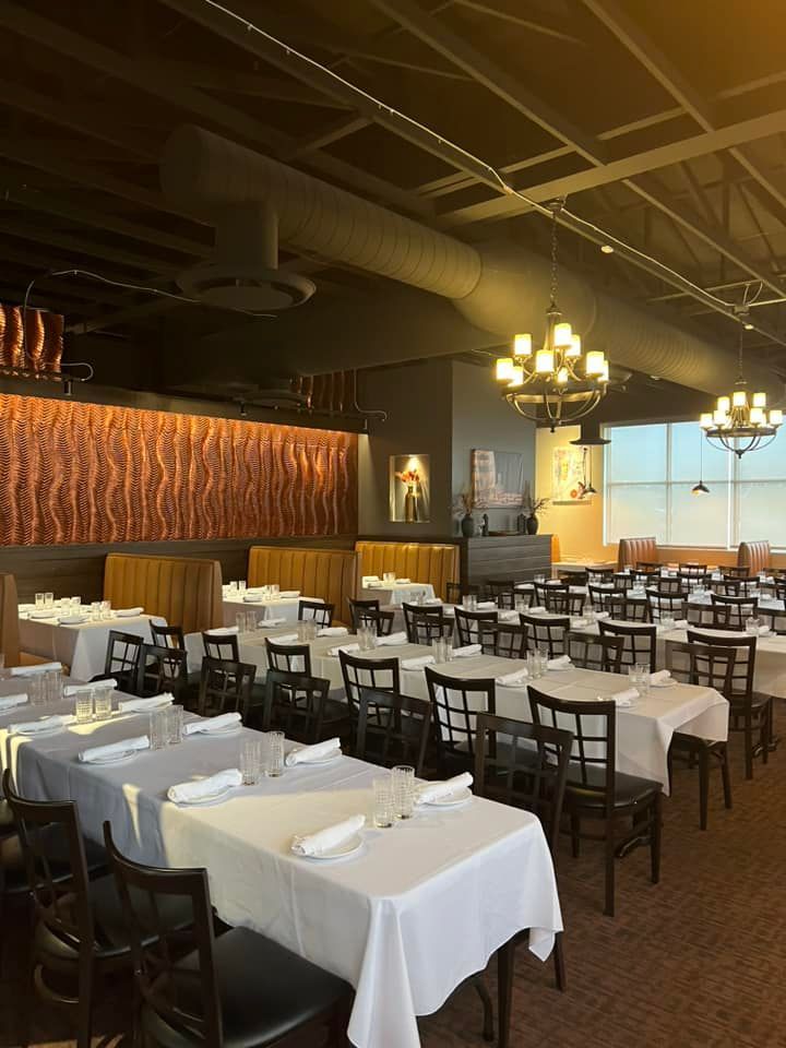 An elegant restaurant dining room featuring rows of tables set with white tablecloths and dark chairs under chandeliers.