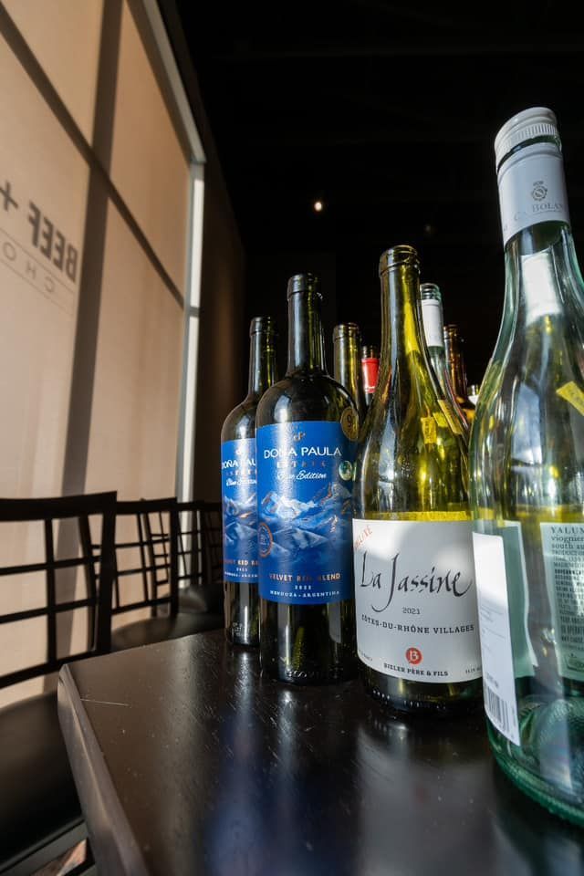 Several wine bottles sit on a table, with focus on labels in blue and white, inside a dimly lit restaurant.