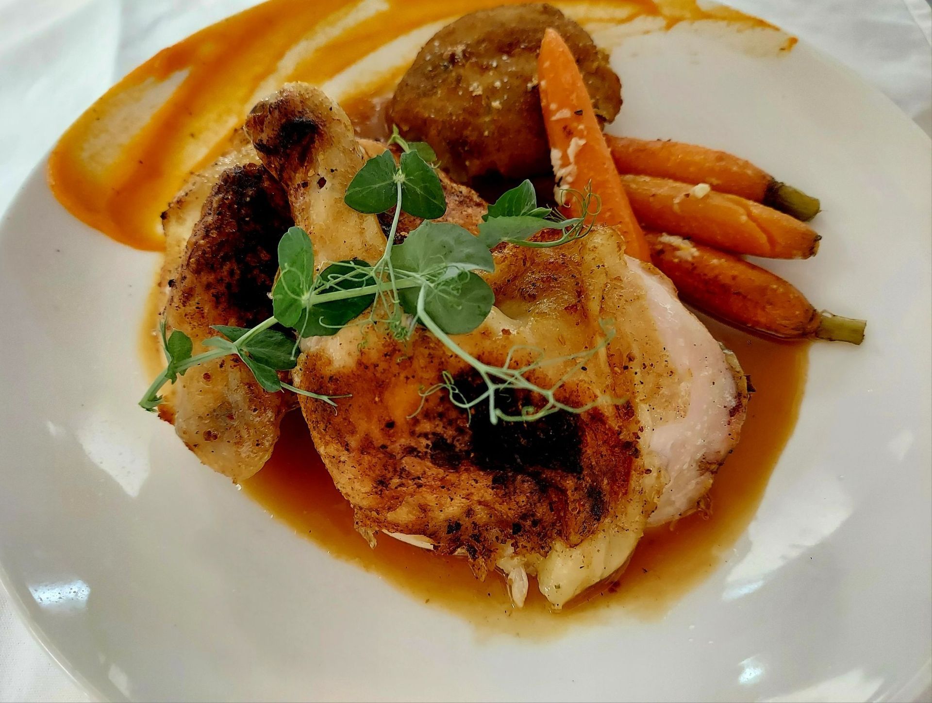 Roasted chicken breast served with glazed baby carrots and a savory sauce on a white plate, garnished with microgreens.
