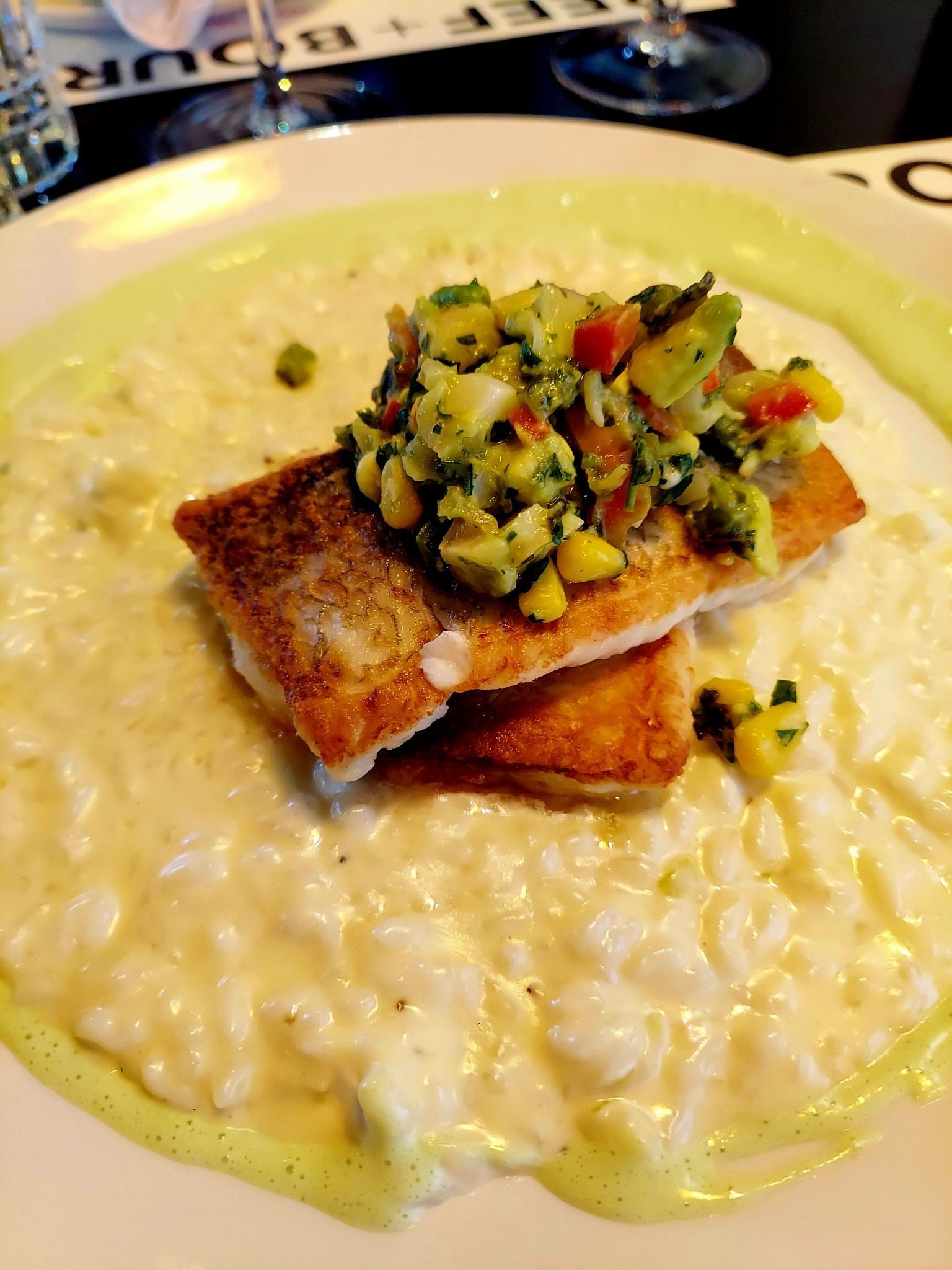 A plate of pan-seared white fish topped with a colorful vegetable salsa, served over a bed of creamy risotto.