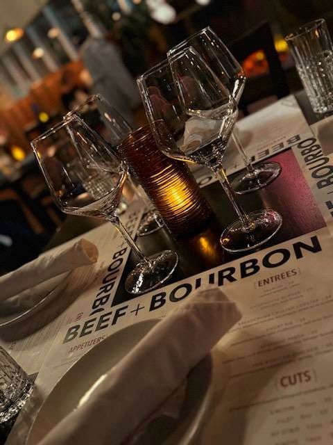 A restaurant table setting with wine glasses, a glowing candle, and a menu titled 