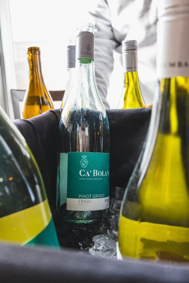 Several wine bottles in a dark cooler filled with ice, featuring a central bottle labeled 