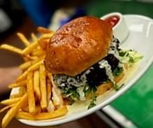 A burger topped with greens and sauce, served with golden french fries and a side of red dipping sauce on a white plate.