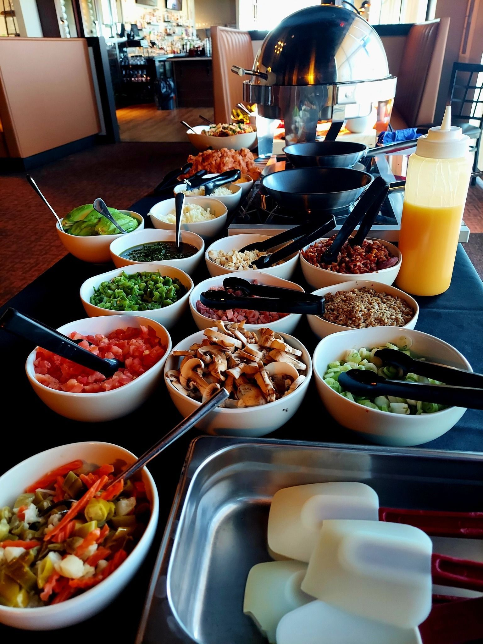 A buffet spread featuring various bowls of fresh ingredients and toppings for a meal, with cooking utensils nearby.
