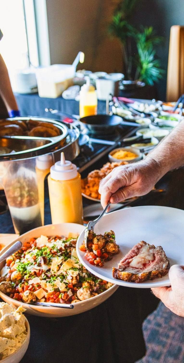 A person uses a fork to plate a slice of meat and a side dish at a food buffet.