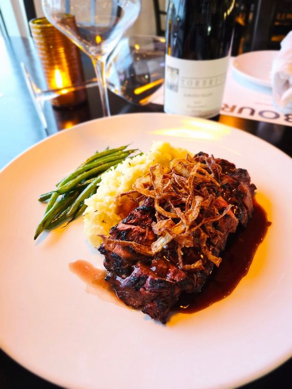 A plate of steak topped with crispy fried onions, served with mashed potatoes and green beans, next to a glass of wine.