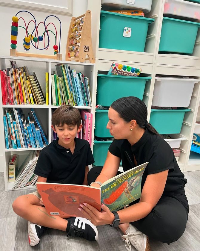 A woman is sitting on the floor reading a book to a young boy.