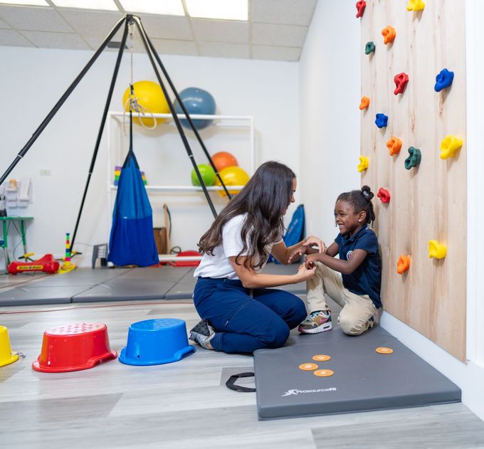 A woman is kneeling next to a child in front of a climbing wall