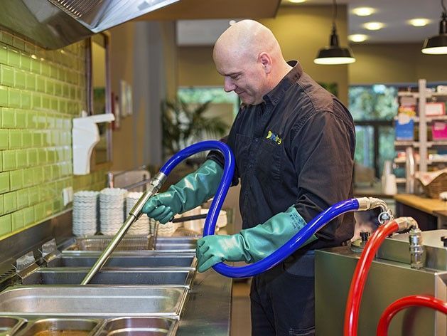 Ein Servicemitarbeiter saugt das Frittieröl aus der Fritteuse, damit es in der Filtermaschine gefiltert werden kann.