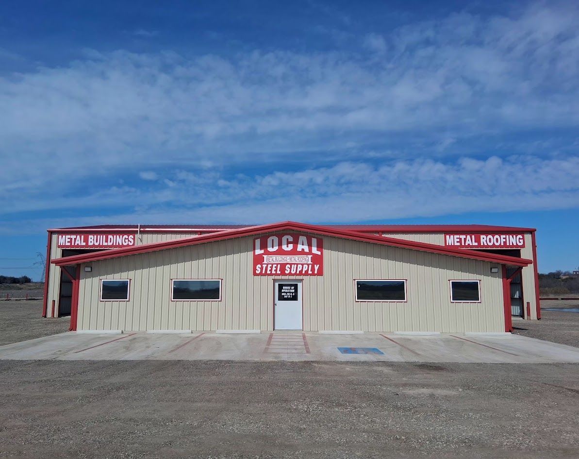 Small roadside building with red trim and signs under a blue sky on a gravel lot
