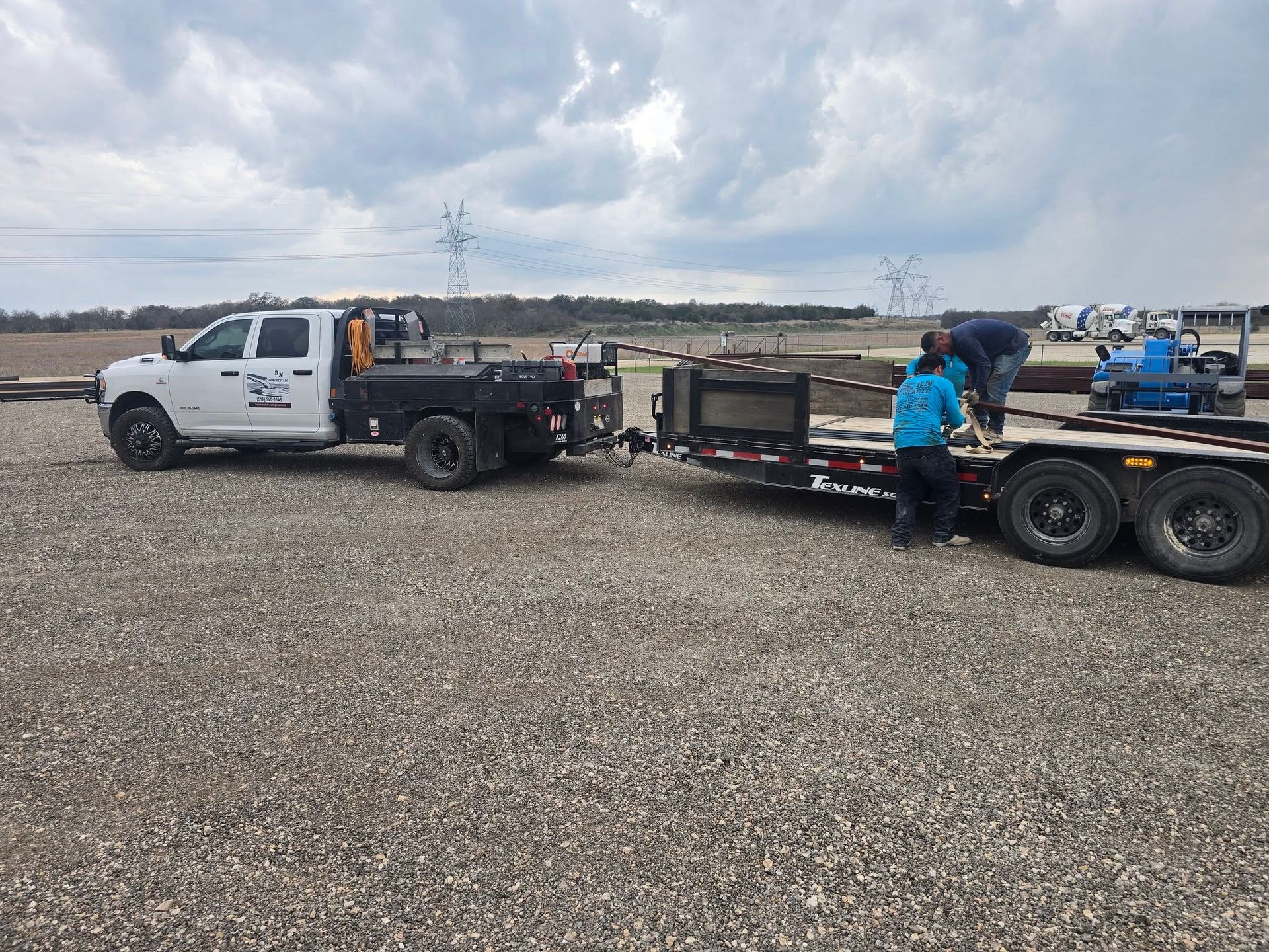 White tow truck with flatbed trailer and workers on a gravel lot under a cloudy sky