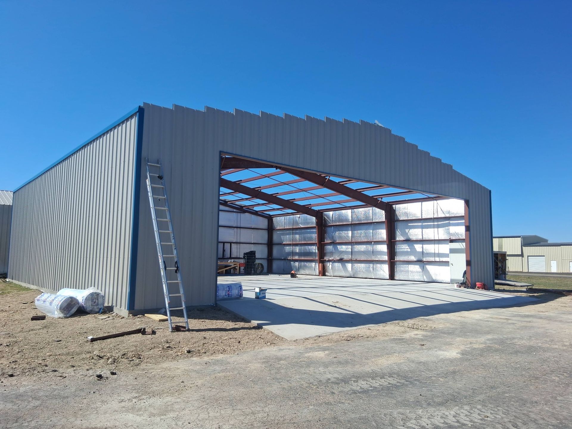 Steel-frame industrial building under construction with open front and gravel foreground