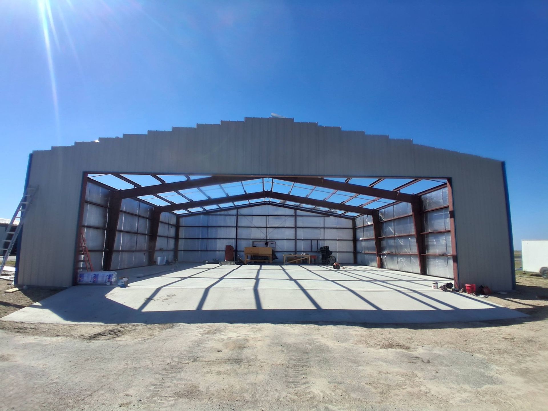 Open warehouse with steel frame and concrete floor under a bright blue sky.